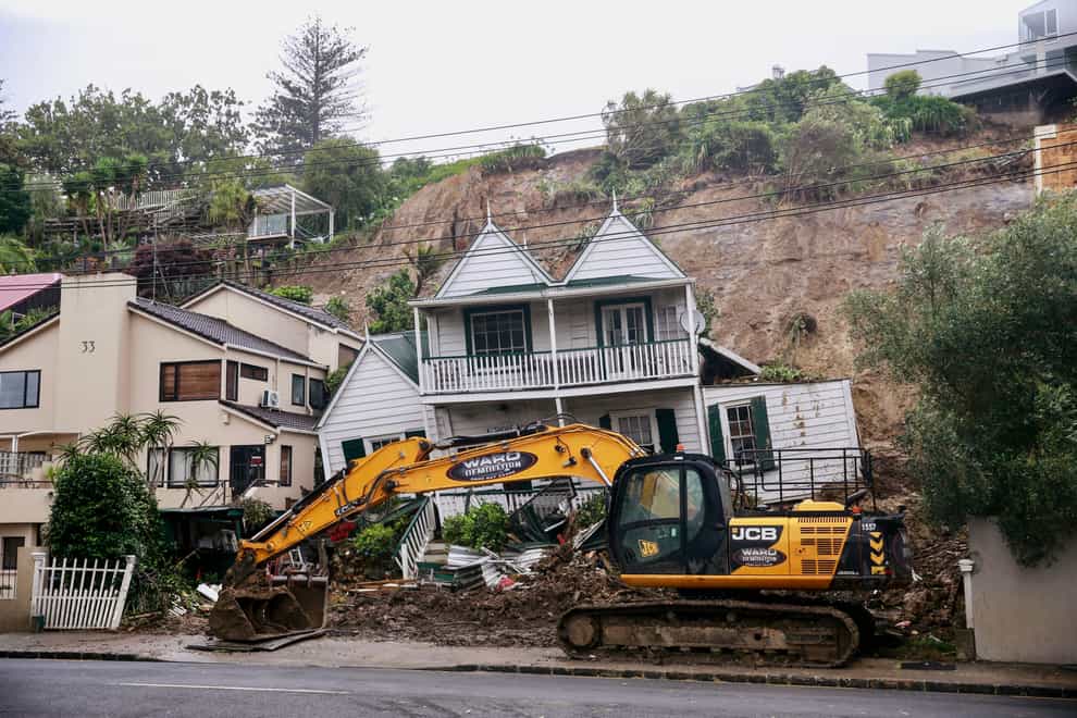 An excavator clears debris at a home badly damaged by flooding and landslides in Auckland (Alex Burton/New Zealand Herald via AP)