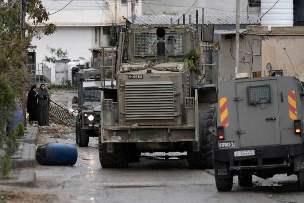 Palestinian women watch Israeli military vehicles in a camp near Jericho (Majdi Mohammed/AP)