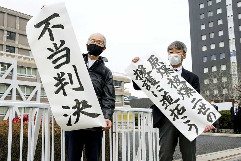 Plaintiff Katsuhiro Hirano, right, and unidentified lawyer for the plaintiffs display signs after a judgement at Hiroshima District Court in Hiroshima (Kyodo News/AP)