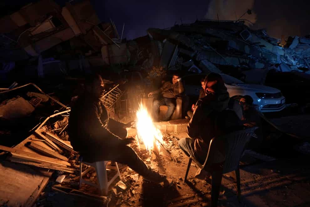 People warm up with fire in front of destroyed buildings in Antakya, southern Turkey (Khalil Hamra/AP)