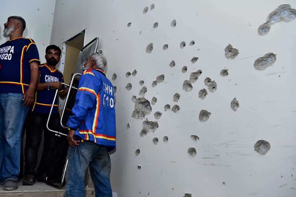 Rescue workers stand beside a bullet-riddled wall (M. Noman/AP)
