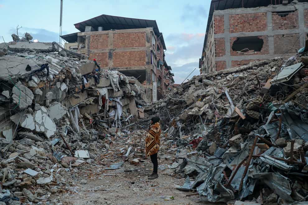 A woman stands among rubble from collapsed buildings, in Hatay, southern Turkey, Saturday, Feb. 11, 2023. Rescue teams using thermal cameras to locate signs of life are continuing to pull survivors out of mounds of rubble, five days after a major earthquake struck a sprawling border region of Turkey and Syria. (AP Photo/Can Ozer)