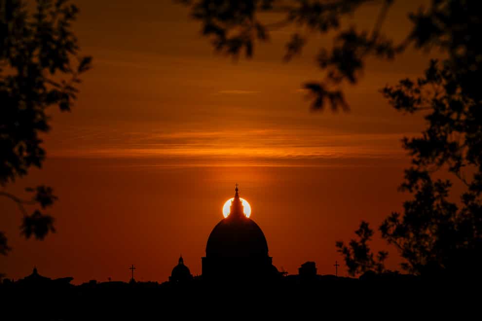The sun sets behind the dome of St Peter’s Basilica in Rome (Andrew Medichini/AP)
