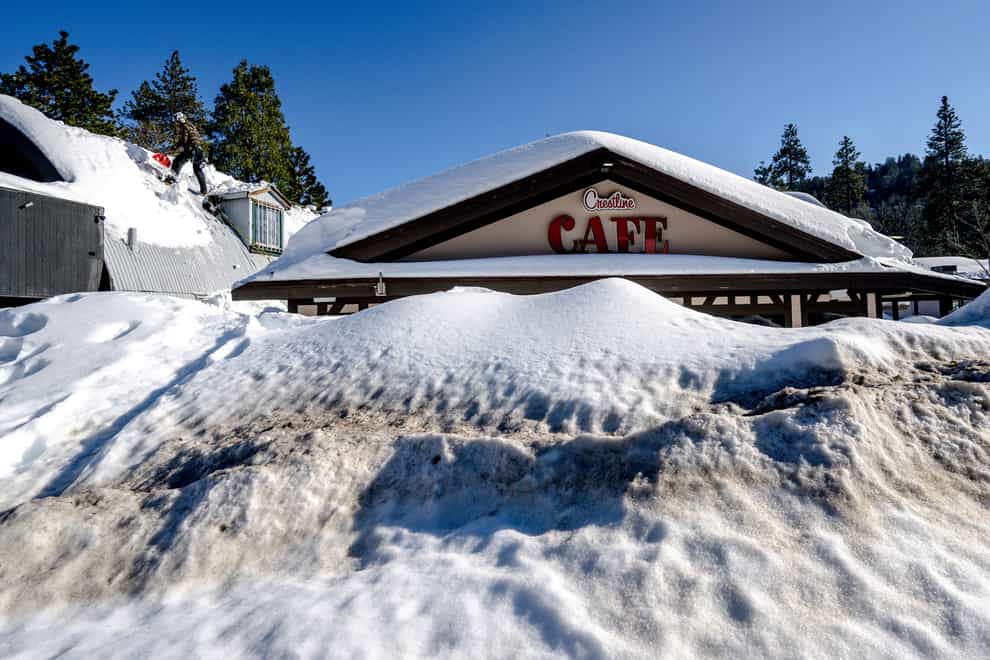 A man shovels snow off the roof of a store in Crestline, California (Watchara Phomicinda/The Orange County Register via AP)