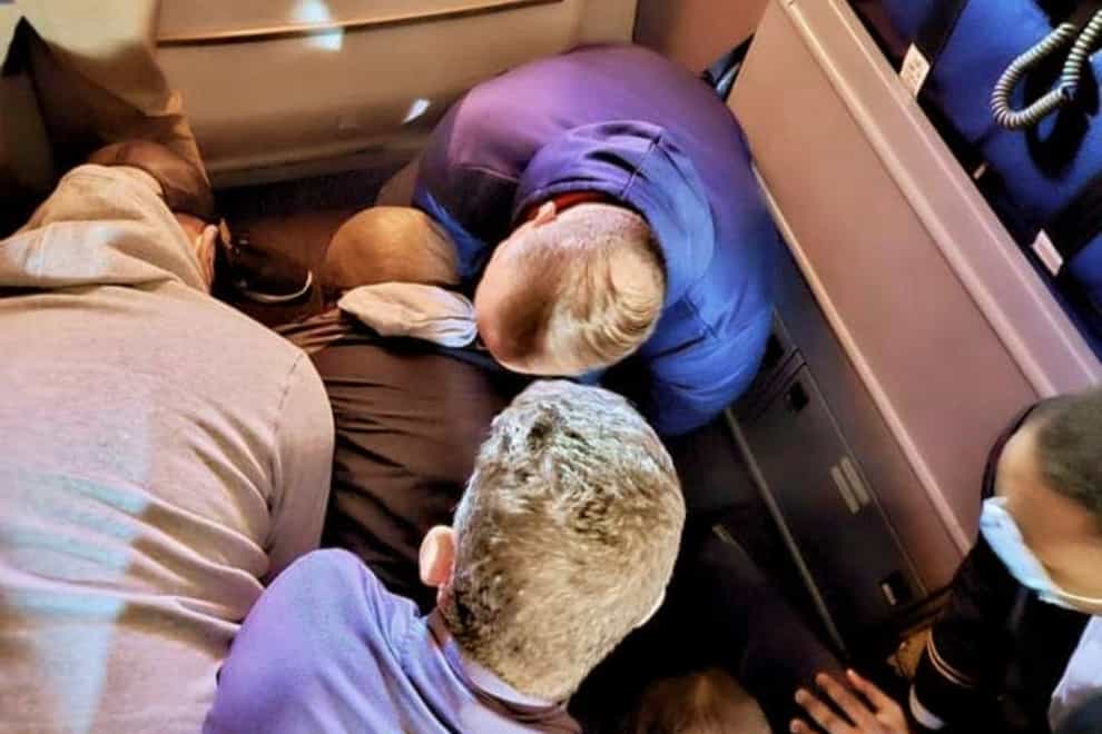 Passengers and crew members restraining a man who, according to federal authorities, tried to open an airliner’s emergency door and stab a flight attendant (Simik Ghookasian/AP)