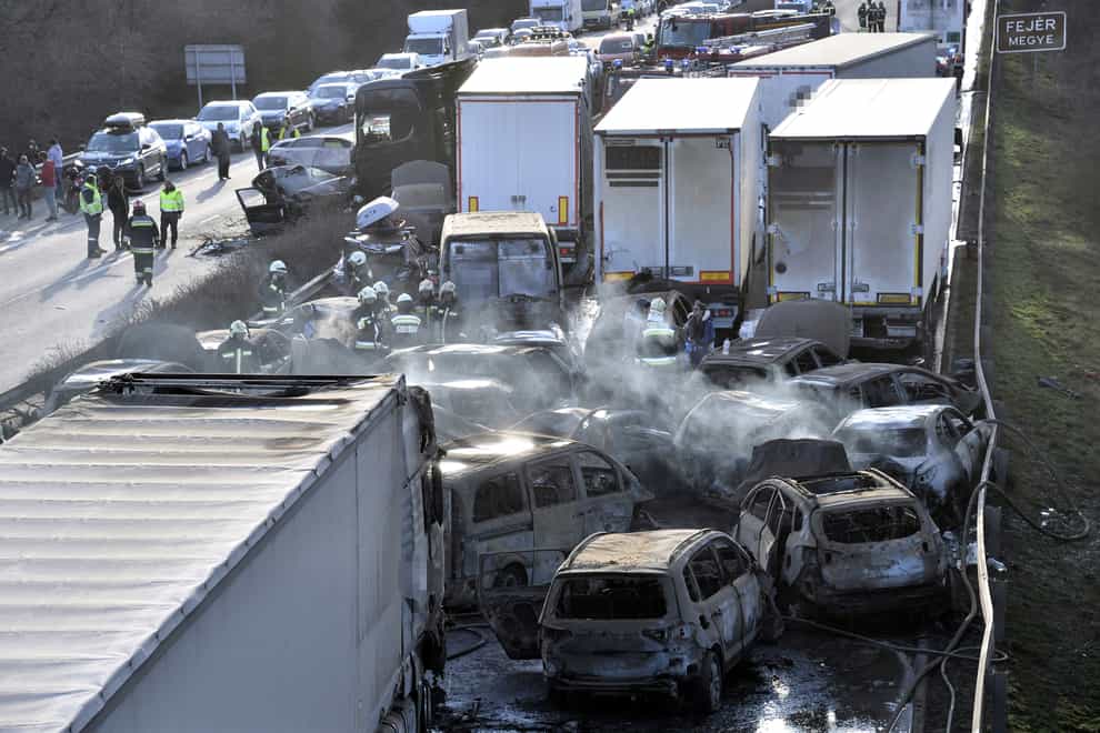 Firefighters work among smouldering cars after several trucks and cars crashed on M1 motorway near Herceghalom, Hungary (MTI via AP)