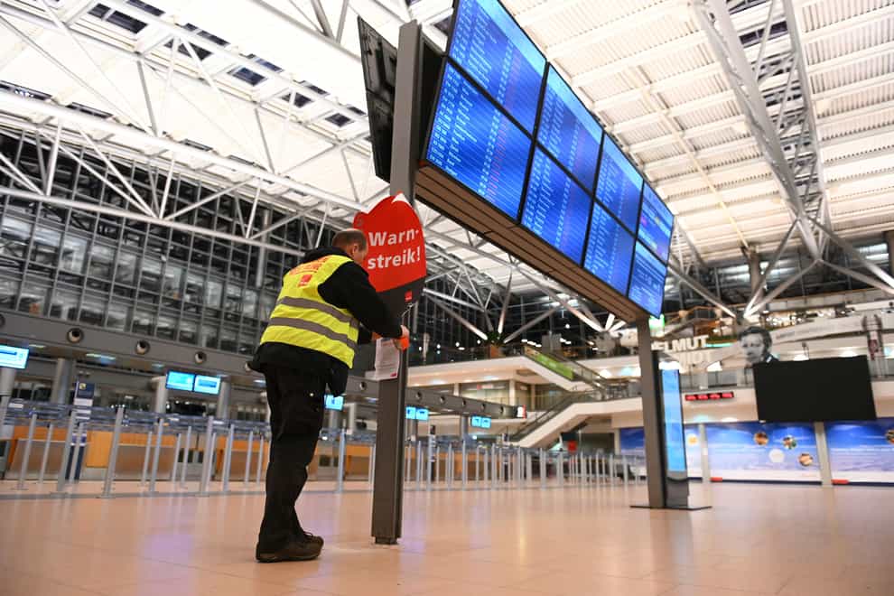 A union representative sticks a poster reading ‘Warning strike!’ and a flyer on the display board in the empty Terminal 2 at Hamburg Airport (dpa via AP)