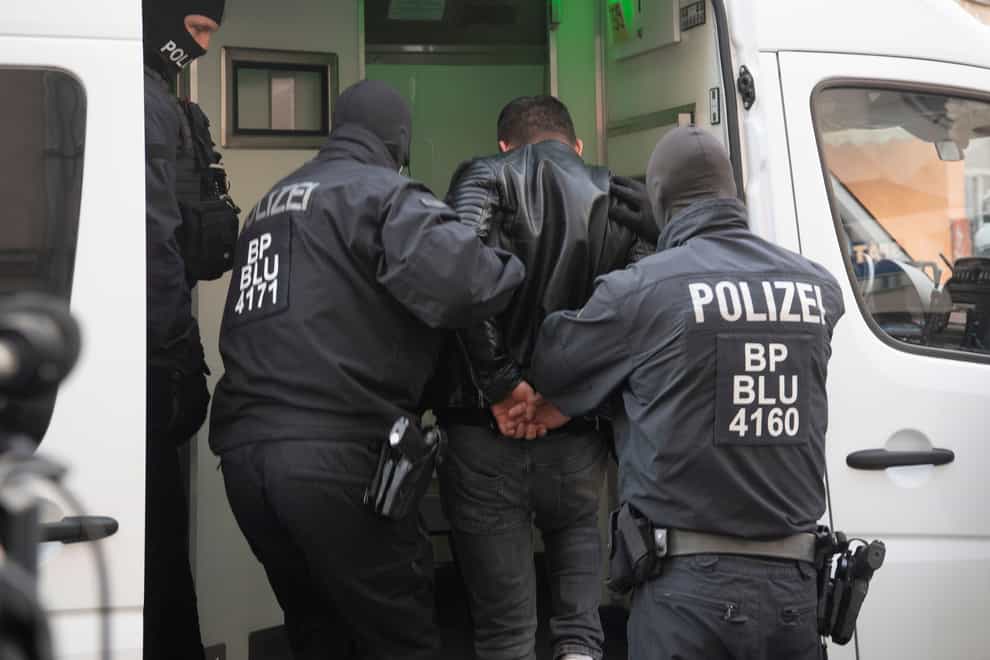Police officers conduct a man during a raid in Berlin, Germany (dpa via AP)