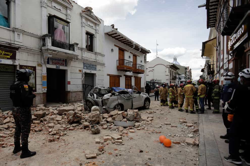 Rescue workers stand next to a car crushed by debris after an earthquake in Cuenca, Ecuador, Saturday, March 18, 2023.. The U.S. Geological Survey reported an earthquake with a magnitude of 6.7 about 50 miles south of Guayaquil (Xavier Caivinagua/AP/PA)