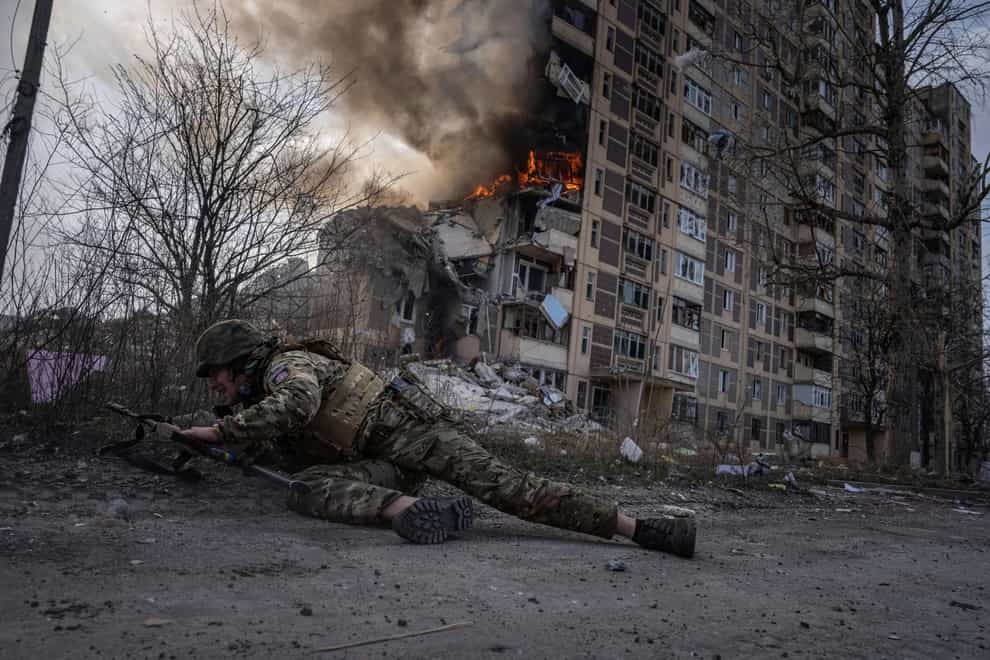 A Ukrainian police officer takes cover in front of a burning building hit in a Russian airstrike in Avdiivka (Evgeniy Maloletka/AP)