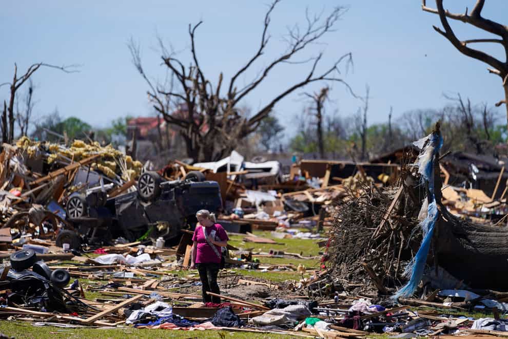 A woman walks near an uprooted tree and debris from homes damaged by a tornado (Julio Cortez/AP)