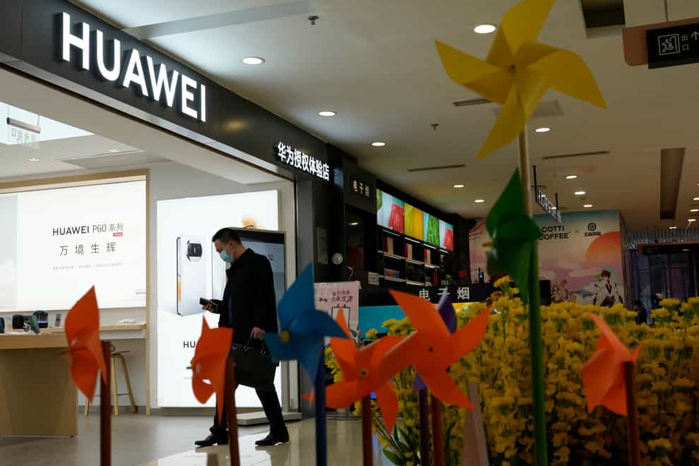 A man walks past a bed of plastic flowers outside the Huawei shop in Beijing (Ng Han Guan/AP)