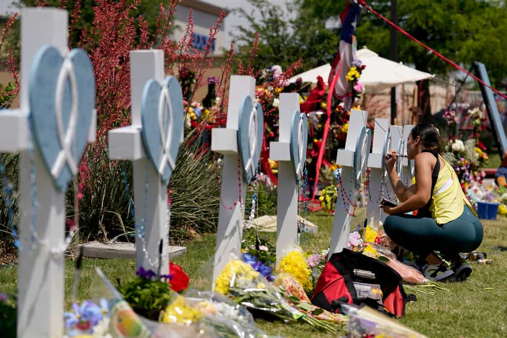 A woman signs a cross that stands by others at a makeshift memorial (Tony Gutierrez/AP)