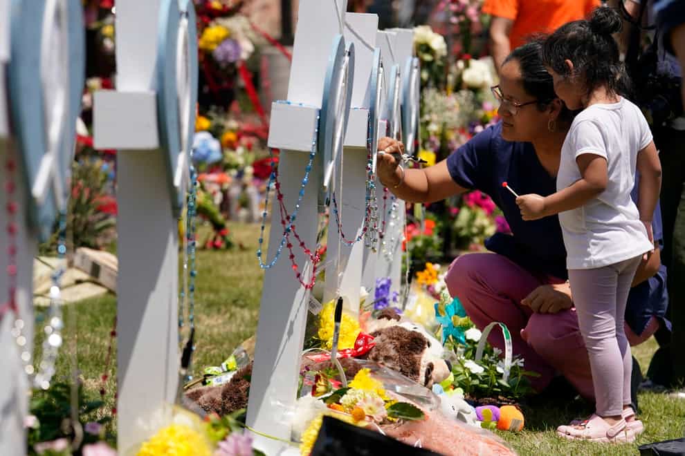 A woman signs a cross as a child looks on at a makeshift memorial by the mall where several people were killed in Saturday’s mass shooting, Monday, May 8, 2023, in Allen, Texas. (AP Photo/Tony Gutierrez)