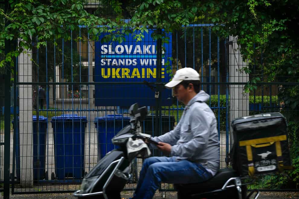 A delivery rider moves past a billboard showing a support for Ukraine on display in between fences at the Slovakia Embassy in Beijing (AP Photo/Andy Wong)