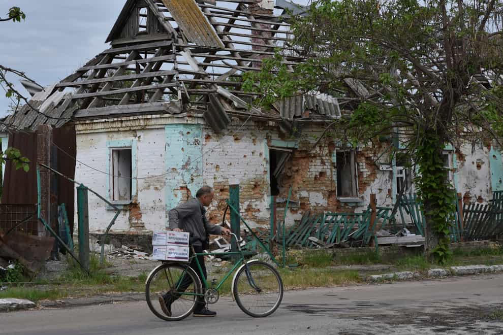 A local man hauls a bicycle with humanitarian aid in front of a house which was destroyed by Russian shelling in Orihiv, Ukraine (Andriy Andriyenko/AP)