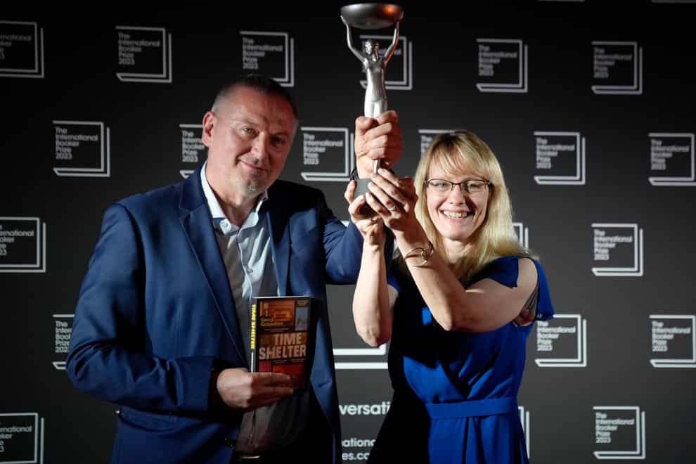 Bulgarian writer Georgi Gospodinov, left, holds up the winner’s trophy after his book Time Shelter translated from Bulgarian by Angela Rodel, right, won The International Booker Prize 2023, in London, Tuesday, May 23, 2023 (Kirsty Wigglesworth/PA)