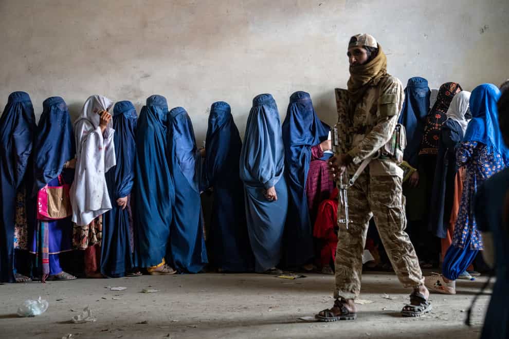 A Taliban fighter stands guard as women wait to receive food rations distributed by a humanitarian aid group, in Kabul (AP)