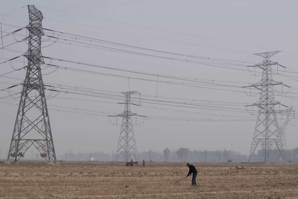 A farmer tills his land under power lines near central China’s Henan province (Ng Han Guan/AP)