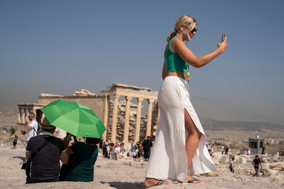 A tourist takes a selfie as a couple sit under an umbrella in front of the Acropolis (AP Photo/Petros Giannakouris)