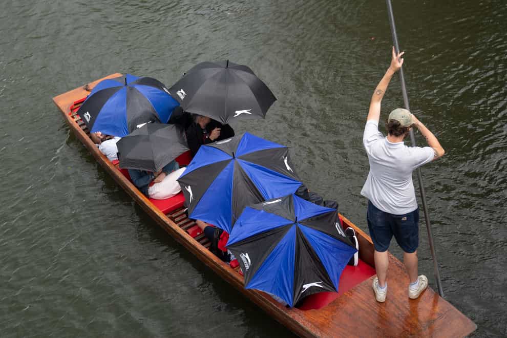 People shelter from the rain under umbrellas as they punt along the River Cam in Cambridge (Joe Giddens/PA)
