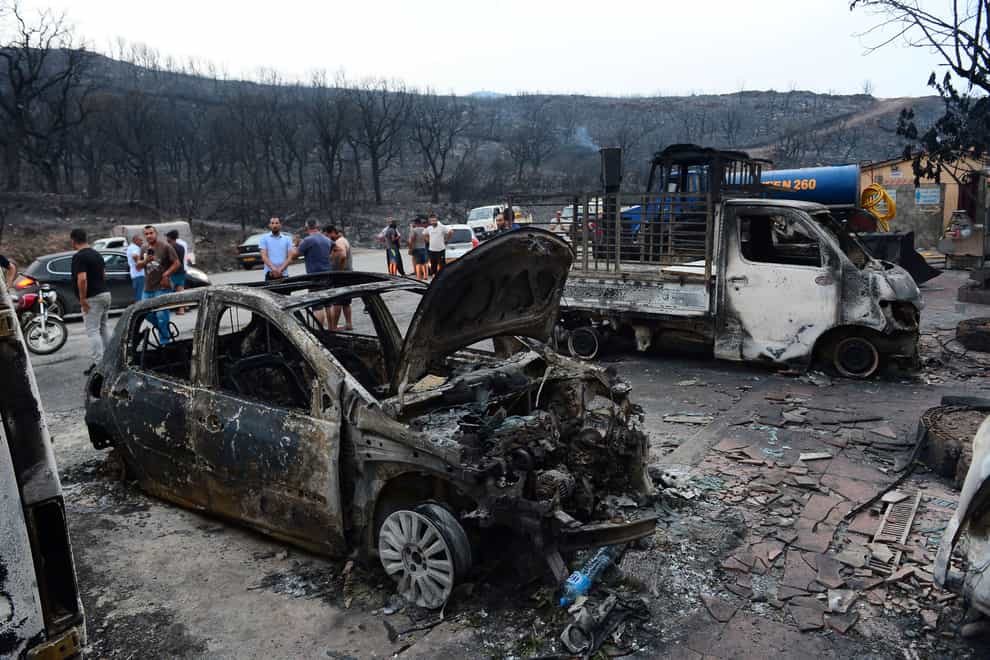 People inspect burnt vehicles after raging wildfires in Bouira, Algeria (AP)
