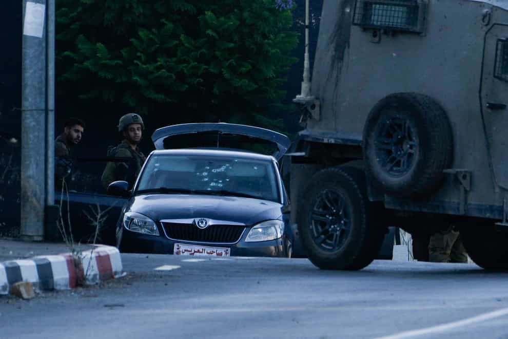 Israeli soldiers stand by a car used by three alleged Palestinian gunmen (Majdi Mohammed/AP)