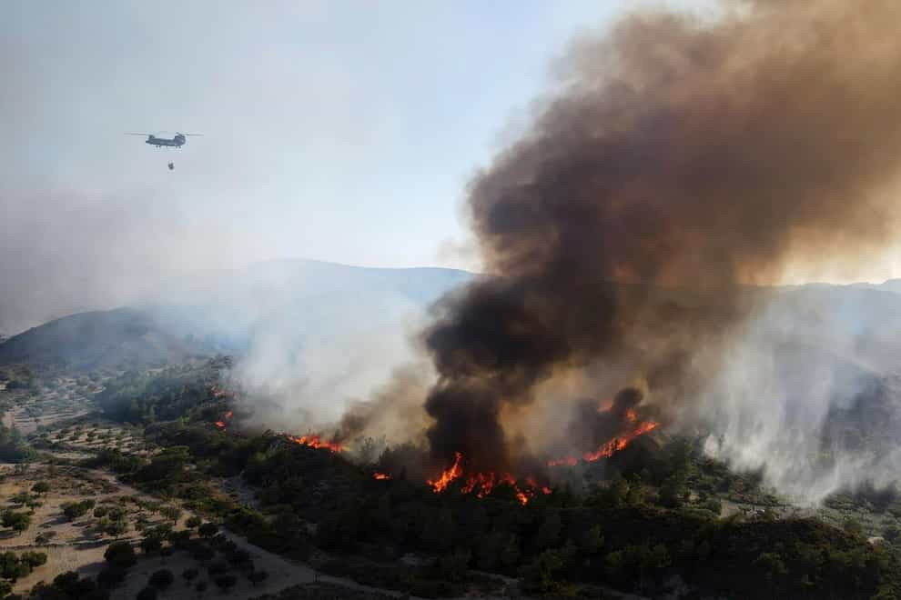 A military helicopter operates as flames burn a forest on the mountains near Vati village, on the Aegean Sea island of Rhodes, southeastern Greece, on Tuesday (Spiros Tsampikakis/AP)
