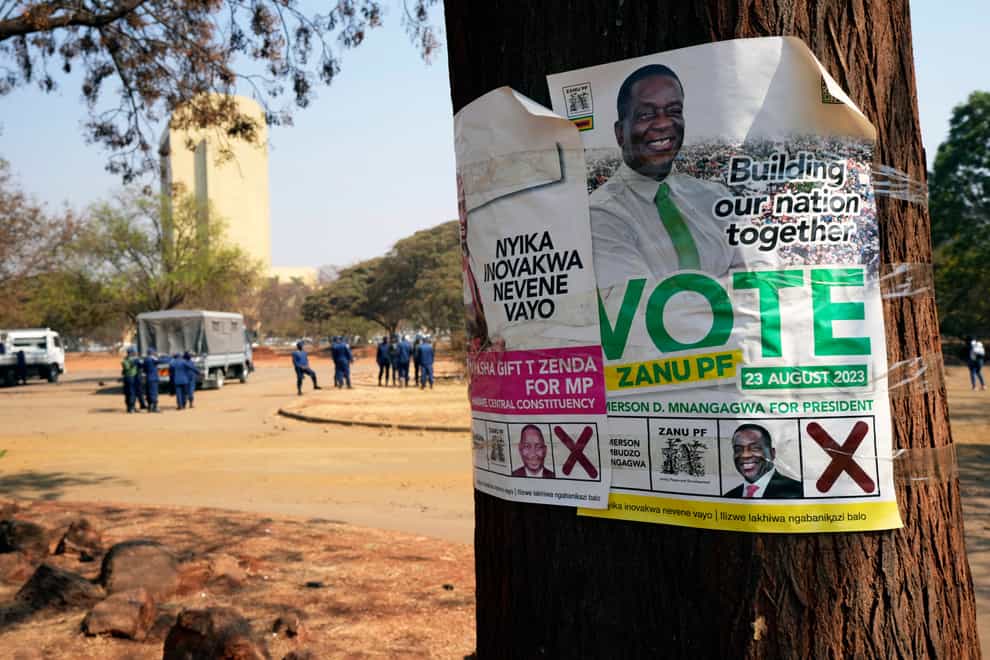 An election campaign poster with a picture of Zimbabwean President Emmerson Mnangagwa on a tree while, in the background, armed riot police prepare to be deployed on the streets of Harare (AP Photo/Tsvangirayi Mukwazhi)