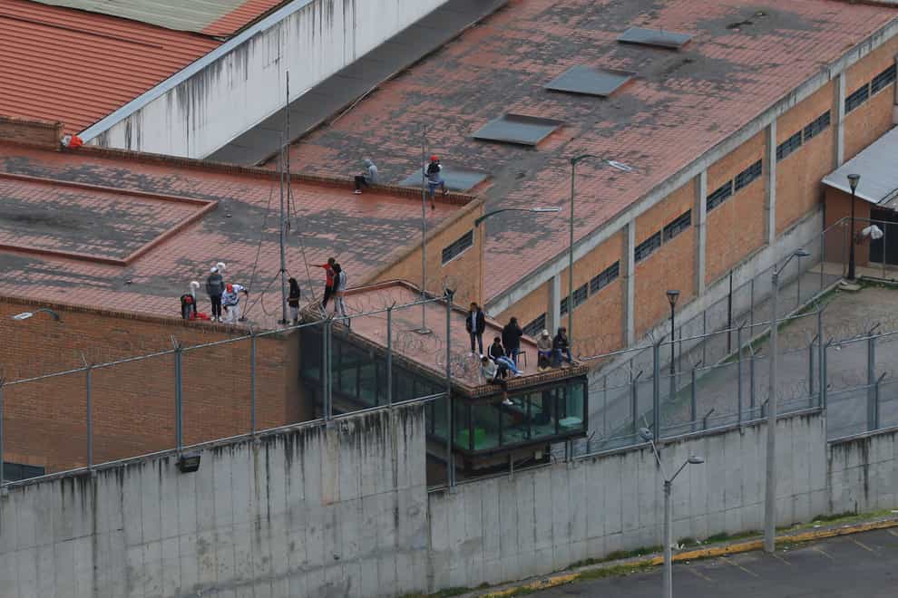 Prisoners stand on the roof of the Turi jail where dozens of prison guards and police officers have been kidnapped by the inmates (AP)