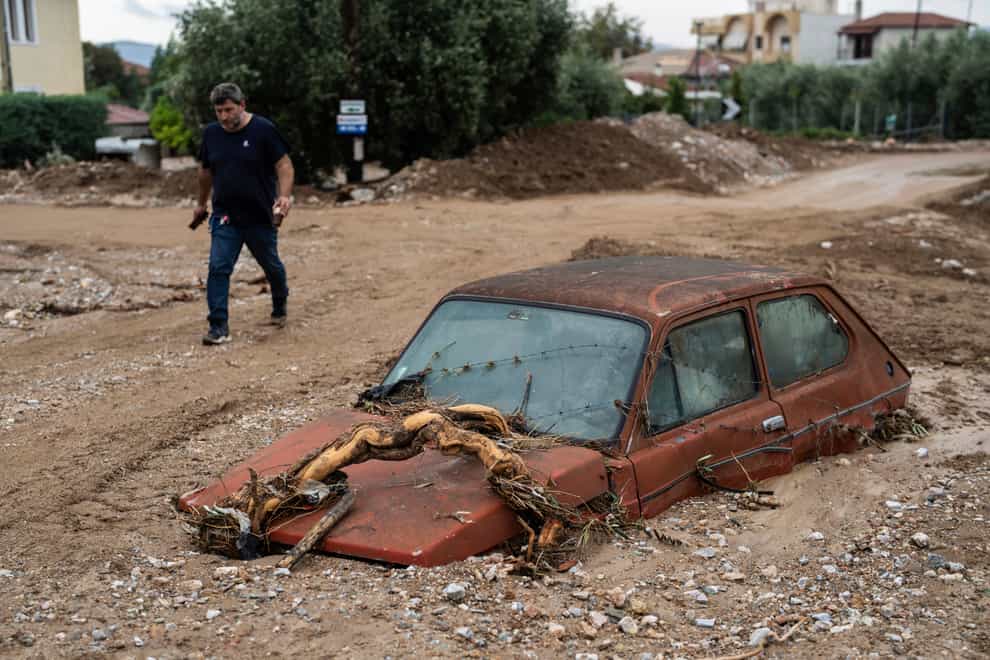 A man walks next to a damaged car after floods in the town of Agria near the city of Volos, Greece (Petros Giannakouris/AP)