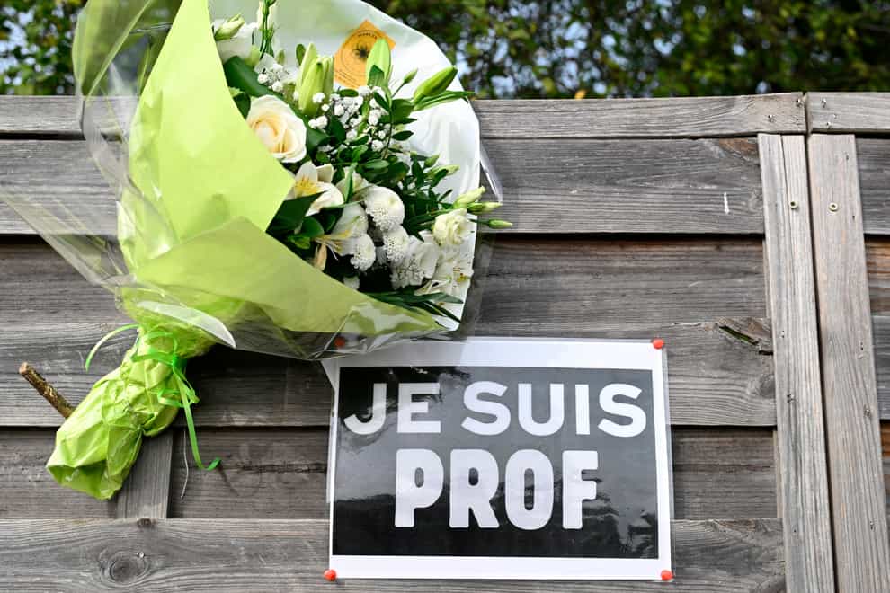 Flowers next to a placard reading ‘I am a teacher’ in tribute to Samuel Paty (Bertrand Guay, Pool via AP)
