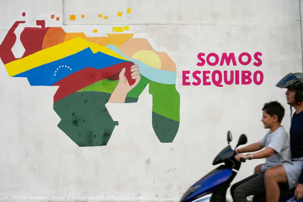 A boy drives a motorcycle in front of a mural of the Venezuelan map with the Essequibo territory included in Caracas, Venezuela (Matias Delacroix/AP)