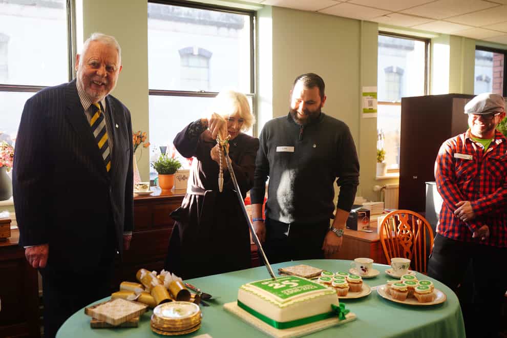 Queen Camilla cuts a cake with a sword from the Lord-Lieutenant of the County and City of Bristol as she joins celebrations for the 25th anniversary of Emmaus Bristol (PA)