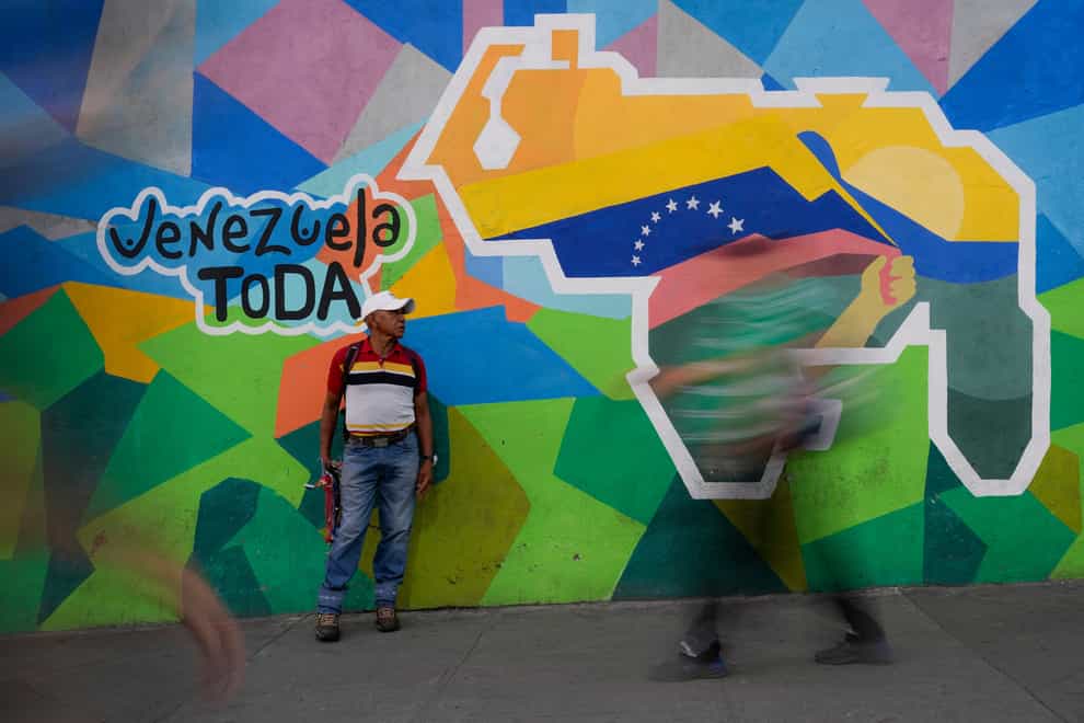 A man sells phone cables in front of a mural of the Venezuelan map with the Essequibo territory included (Matias Delacroix/AP)