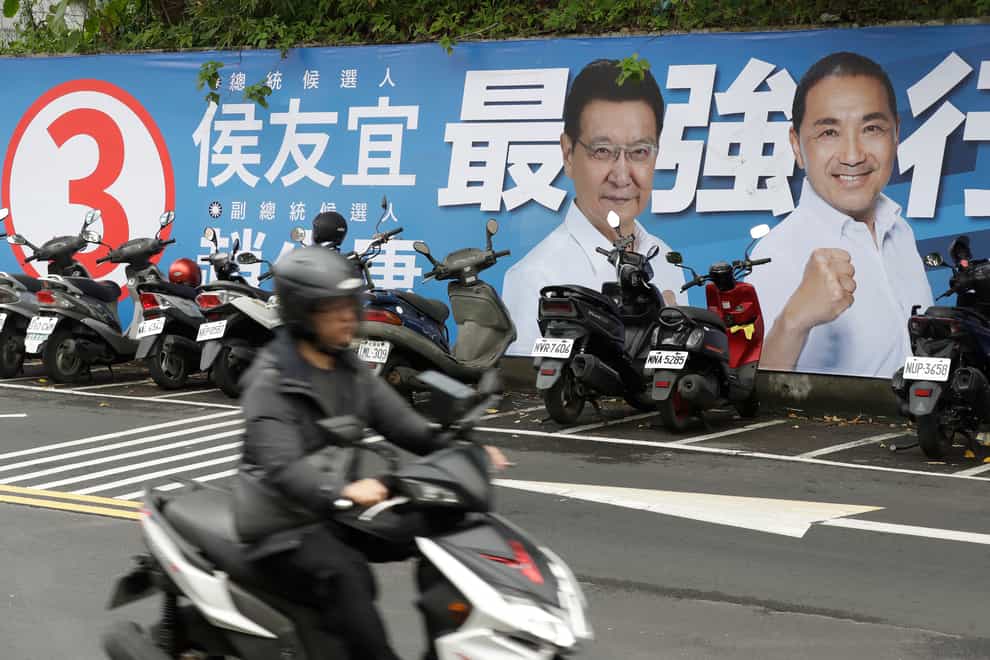 People pass by a poster of candidates running for the Taiwanese presidential election (Chiang Ying-ying/AP)