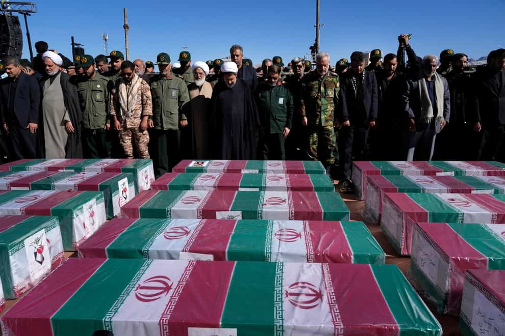 People pray over the flag-draped coffins of victims during their funeral ceremony in the city of Kerman on Friday (Vahid Salemi/AP)
