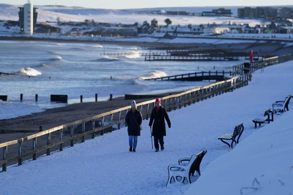 People walk along a snow-covered beach front in Aberdeen as a yellow weather warning remains in place for snow and ice (Andrew Milligan/PA)