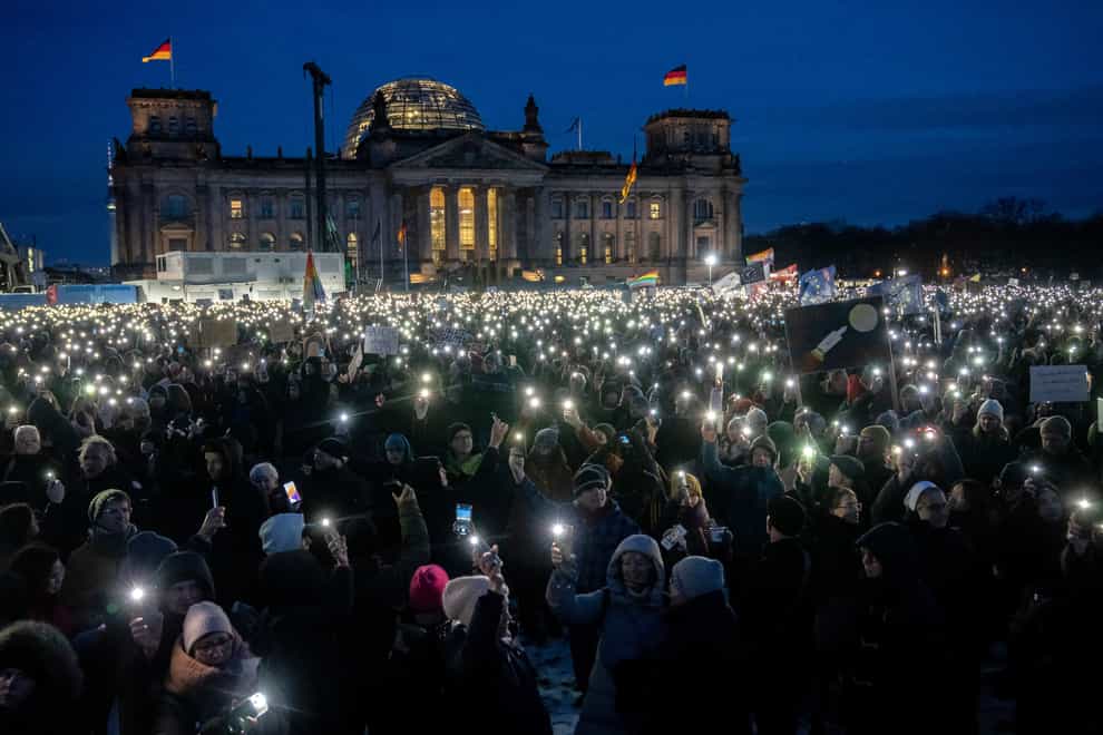 People hold up their phones as they protest against the AfD party and right-wing extremism in front of the Reichstag building in Berlin, Germany (Ebrahim Noroozi/AP)
