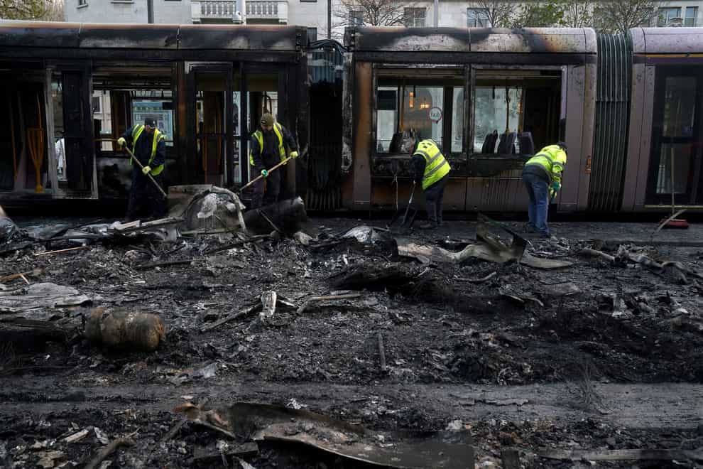 Debris is cleared from a burned out Luas and bus on O’Connell Street in Dublin (PA)