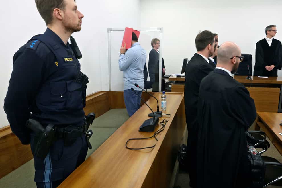 The 31-year-old American man accused of murder stands in the dock behind his lawyers in a courtroom at the district court in Kempten, southern Germany (Karl-Josef Hildenbrand/dpa via AP)