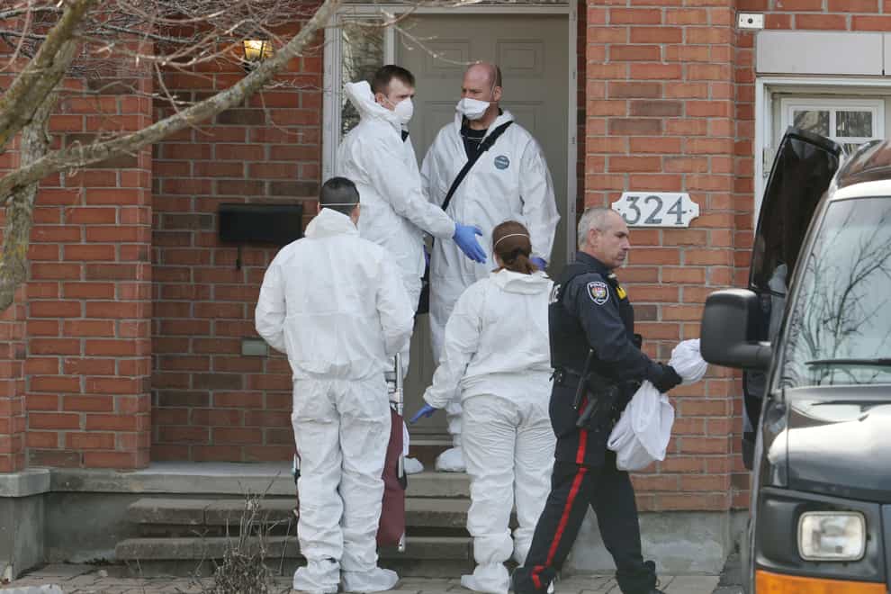 Members of the coroner’s office stand outside the house where the murders occurred (Patrick Doyle/The Canadian Press via AP)