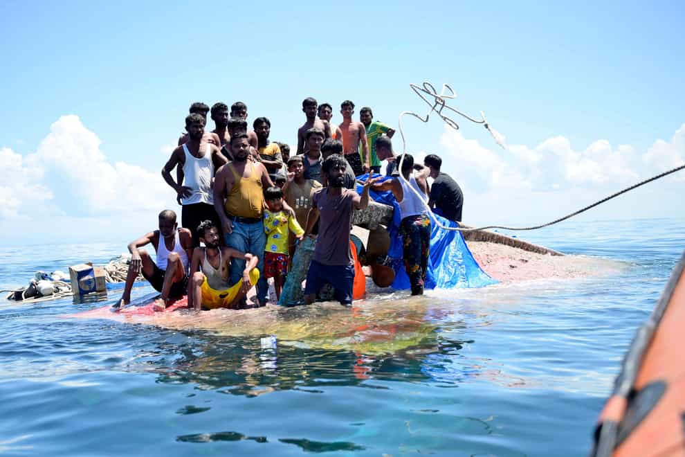 Rohingya refugees stand on their capsized boat as rescuers throw a rope to rescue them in the waters off West Aceh, Indonesia (Reza Saifullah/AP)