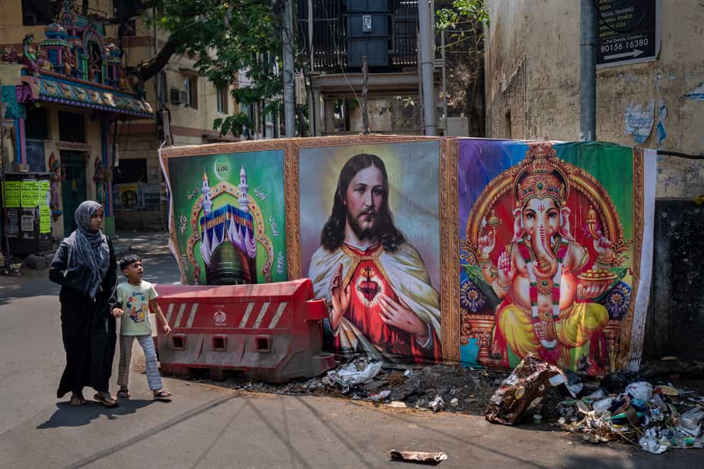 A Muslim woman and a boy walk past portraits of elephant-headed Hindu God Ganesha, Jesus Christ and Islam’s holy sites of Mecca and Medina, in the southern Indian city of Chennai (Altaf Qadri/AP)